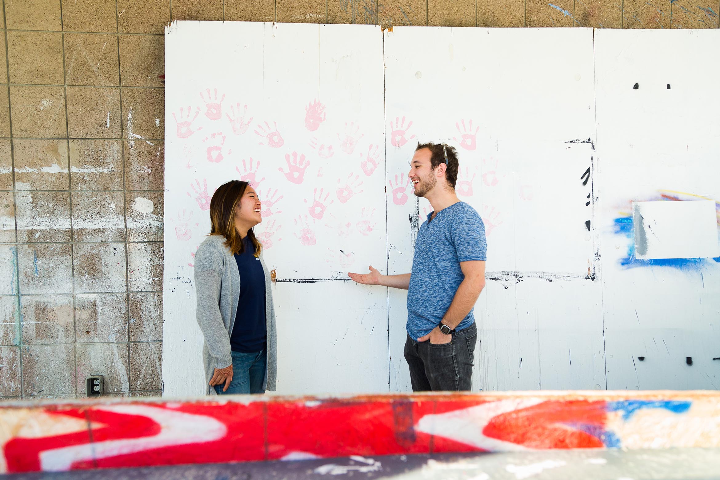 This is an image of two students chatting in front of an art mural.
