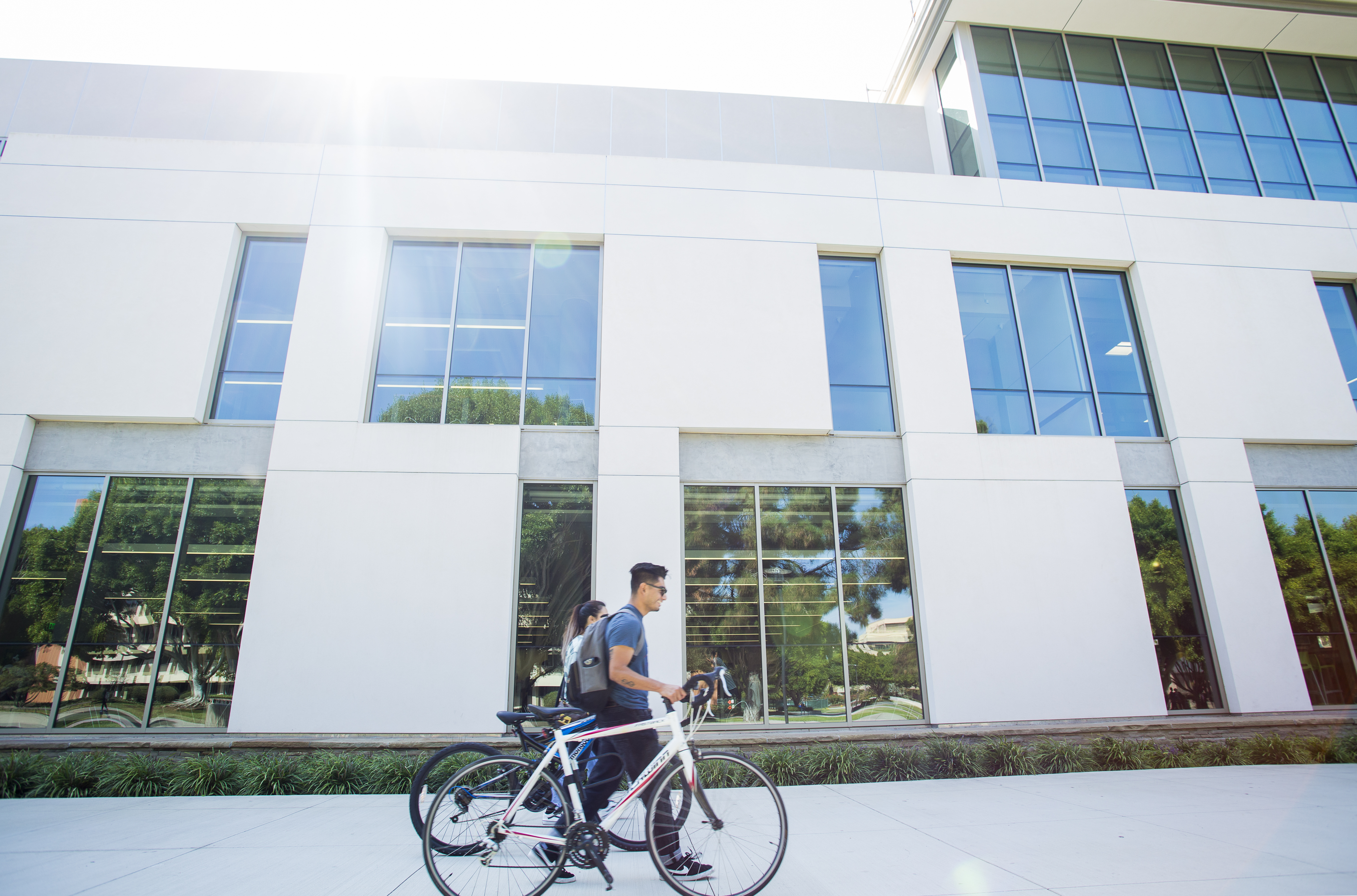 Two students are walking their bikes past the UCSB Library.